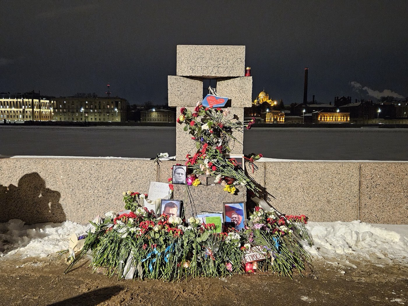 Flowers and photographs of Navalny at a stone memorial on a river embankment at night